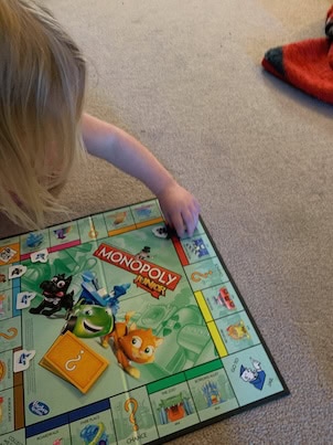 Preschool-aged child playing Monopoly Junior on the floor, using board games to support early math, turn-taking, and play-based learning at home.