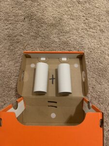 A view of the Adding Machine from the top. The shoe box is laying on the ground open. On the inside of the lid are two toilet paper rolls glued on. On either side of the toilet paper rolls there is a small velcro circle for the numbers to be velcroed onto. There is a plus sign between the toilet paper rolls. There is an equal sign under the plus sign. There is another piece of velcro under the equal sign so that the answer can be attached.