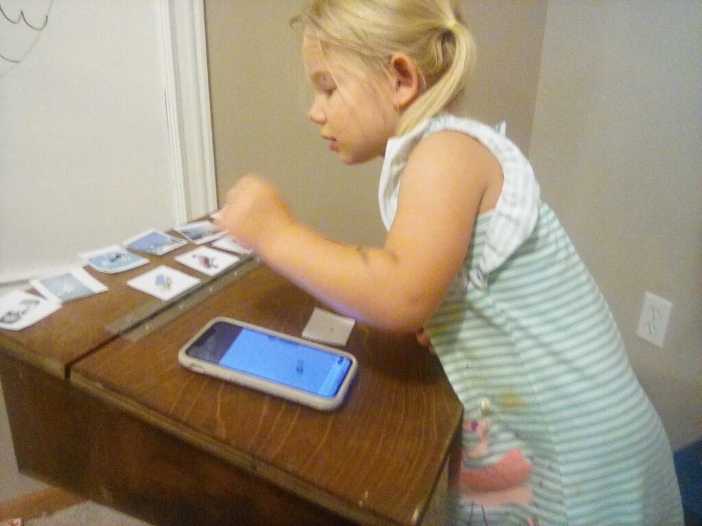 Preschooler playing an educational matching game with picture cards and a phone, engaging in interactive play-based learning at home.