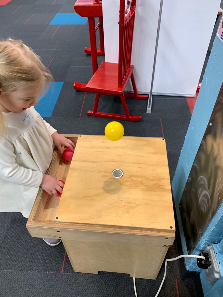 A little girl is playing with a ball STEM table at a museum on a homeschool field trip. She is trying to keep the balls floating in the air.