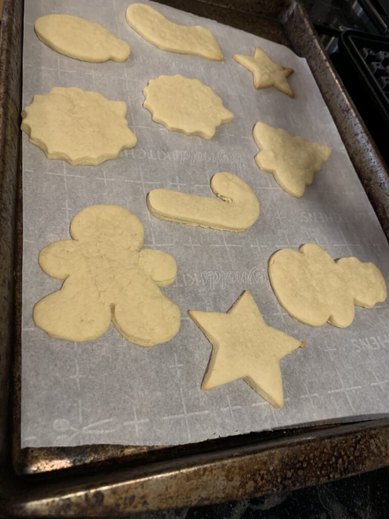 A cookie sheet is covered in parchment paper. On the parchment paper, there are 10 Christmas shaped cookies.