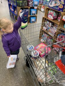 A little girl is putting cheese into a shopping cart at a homeschool field trip to the grocery store.
