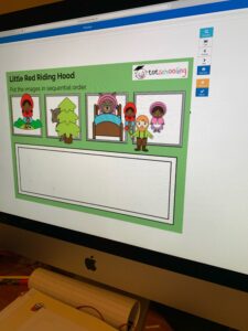 This is an image of a computer screen. On the screen, there is a game being played. The game has four small boxes on top of a larger box. The current game is about Little Red Riding Hood. The child has put all the pictures from the large box into the smaller boxes and placed them in order of the story.