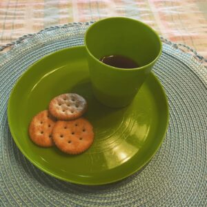 A cup filled with grape juice sits on a plate with three crackers. These are symbols for the Last Supper.