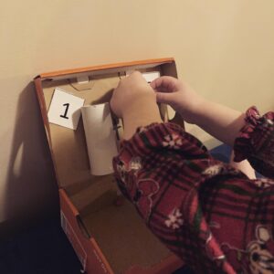 Young child engaging in a hands-on counting activity using a cardboard box, numbered cards, and paper tubes—perfect for play-based learning with toddlers and preschoolers.