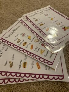 There is a pile of menus from the restaurant dramatic play pack spread out on the floor.