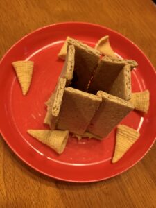 There is a plate with graham crackers put together to look like a wall around a city. There are horn crackers around the "wall" on the plate. There are raisins inside the "wall."