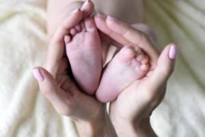 Close-up of a mother's hands gently cradling a newborn's tiny feet, symbolizing care and tenderness during early motherhood. Represents the quiet, nurturing moments that can happen while homeschooling with a newborn.