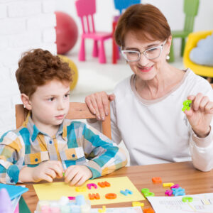 Older female adult helping a rising homeschool kindergartener with language arts skills using colorful letter activities.