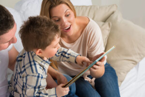 Two parents and child reading together on a couch to build language arts skills for a rising homeschool kindergartener.