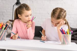 Two young children drawing with colorful pencils and markers at a table, practicing creativity and art skills through process art and project art for preschoolers.