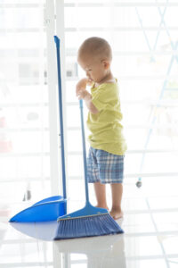 Young child helping with household chores by sweeping the floor with a broom and dustpan, a simple way of teaching kids to serve and build responsibility.