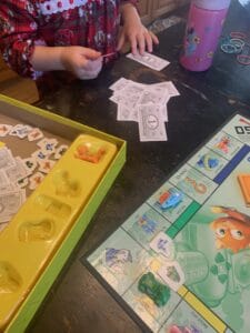 Child playing a kid-friendly board game involving pretend money, game pieces, and character cards—encouraging early math skills and play-based learning for preschoolers.