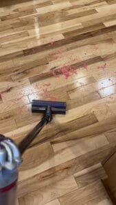 Handheld vacuum cleaning up spilled pink dyed rice from a hardwood floor after sensory play. The image highlights practical cleanup tools used alongside sensory bin products to make sensory play manageable and stress-free.