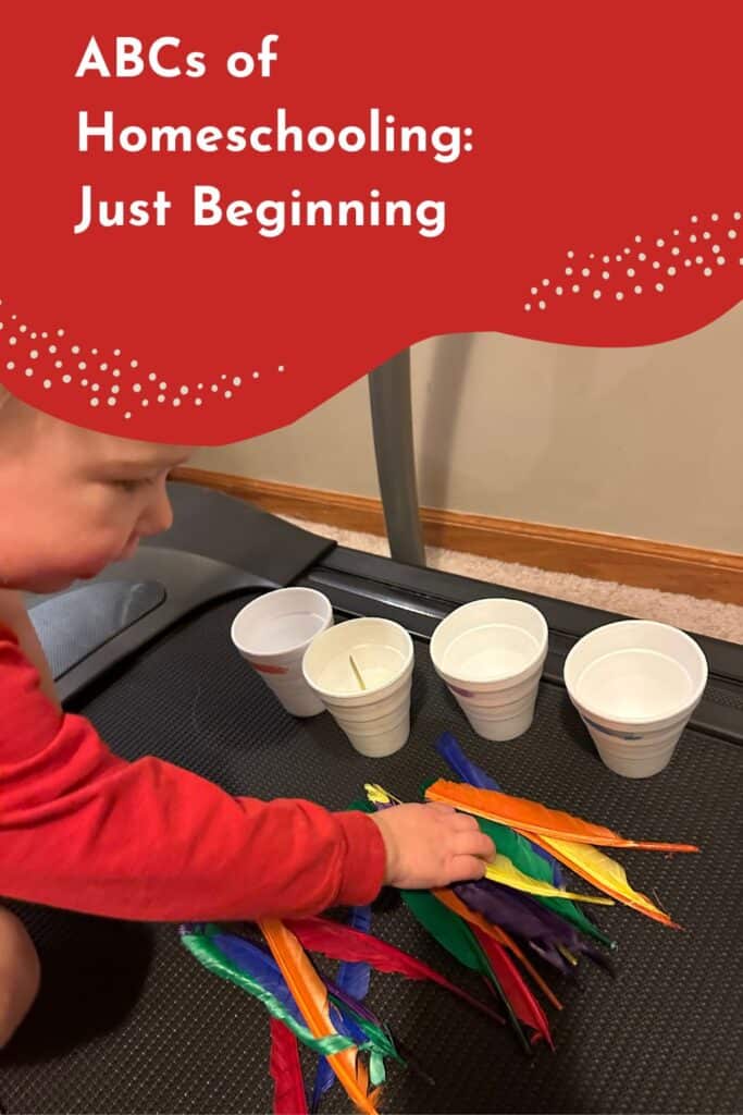 Pinterest image showing a homeschooling toddler preschooler sorting colorful feathers into white cups during a hands-on alphabet learning activity. The image features a young child reaching for bright feathers on a treadmill surface beneath the title "ABCs of Homeschooling: Just Beginning," illustrating an engaging fine motor and early literacy activity for homeschool preschool learning.