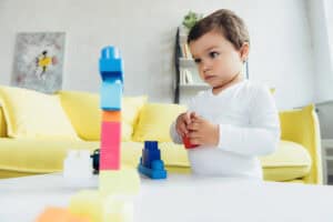 A young child concentrates while stacking colorful building blocks, demonstrating early learning and problem-solving skills that support kindergarten readiness through play.
