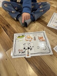 Child in pajamas pointing to a laminated alphabet activity mat featuring the letter C with images like cow, cat, and camel, used to teach letters to toddlers and preschoolers through hands-on phonics practice.