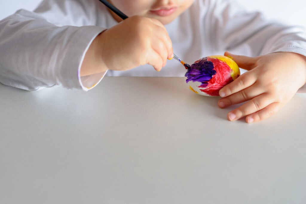 Child painting a rock as part of a nature play activity for preschoolers.