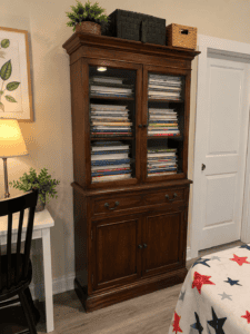 Homeschool organization using a wooden china cabinet filled with homeschool books, workbooks, and curriculum, with storage baskets on top.”