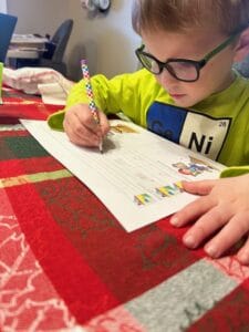 Child sitting at the kitchen table and completing a homeschool worksheet with a pencil.